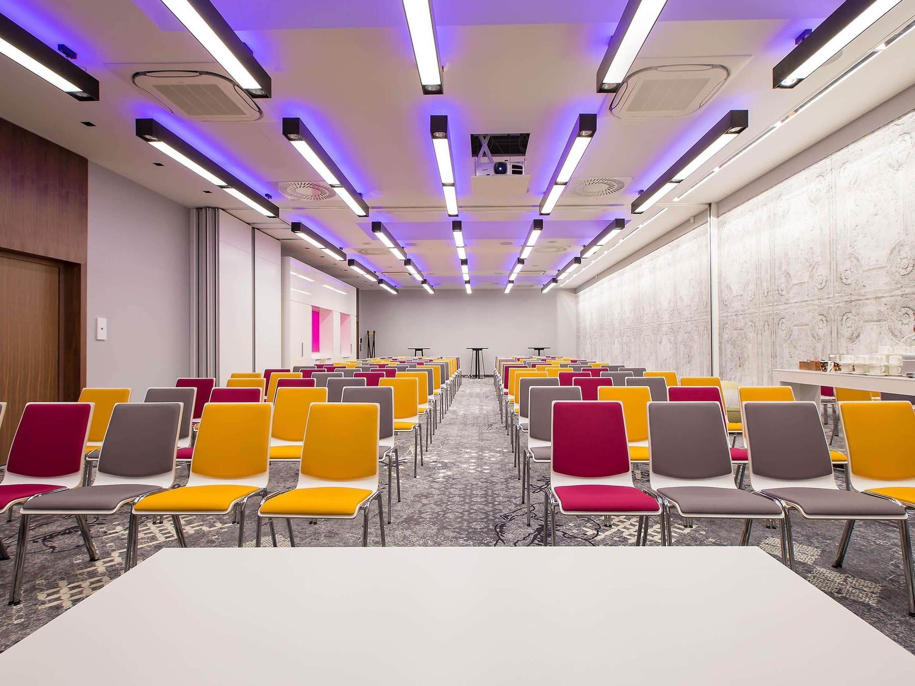 A conference room with rows of chairs, a long table, and a patterned carpet.