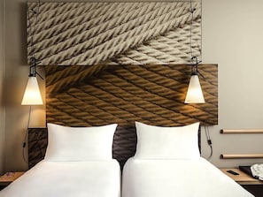 A hotel room with a bed, two bedside lamps, a nightstand, and a wall with a textured pattern. - ibis Saint Quentin En Yvelines Velodrome (Montigny-le-Bretonneux)