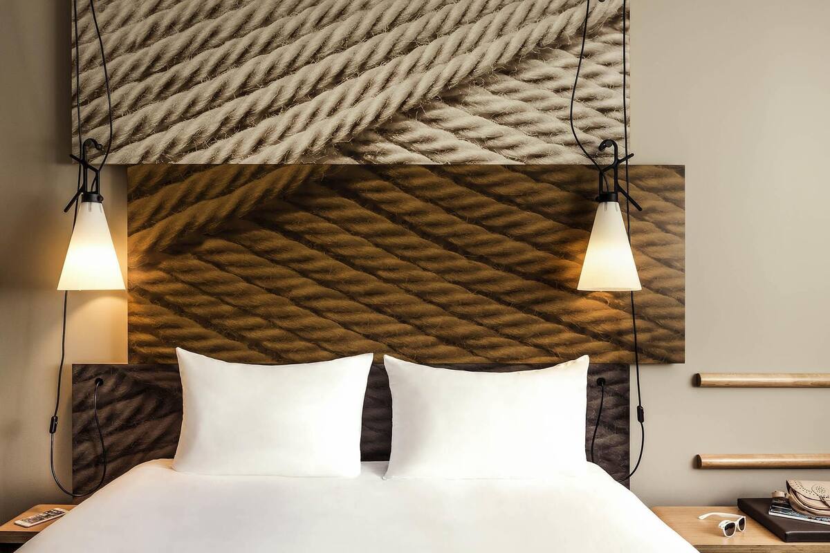 A neatly made bed with white linens, two bedside lamps, and a wall with a textured, woven pattern.
