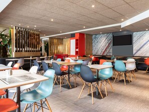 Un intérieur de restaurant moderne avec de nombreuses tables et chaises, un mur d’accent en bois et un grand écran.