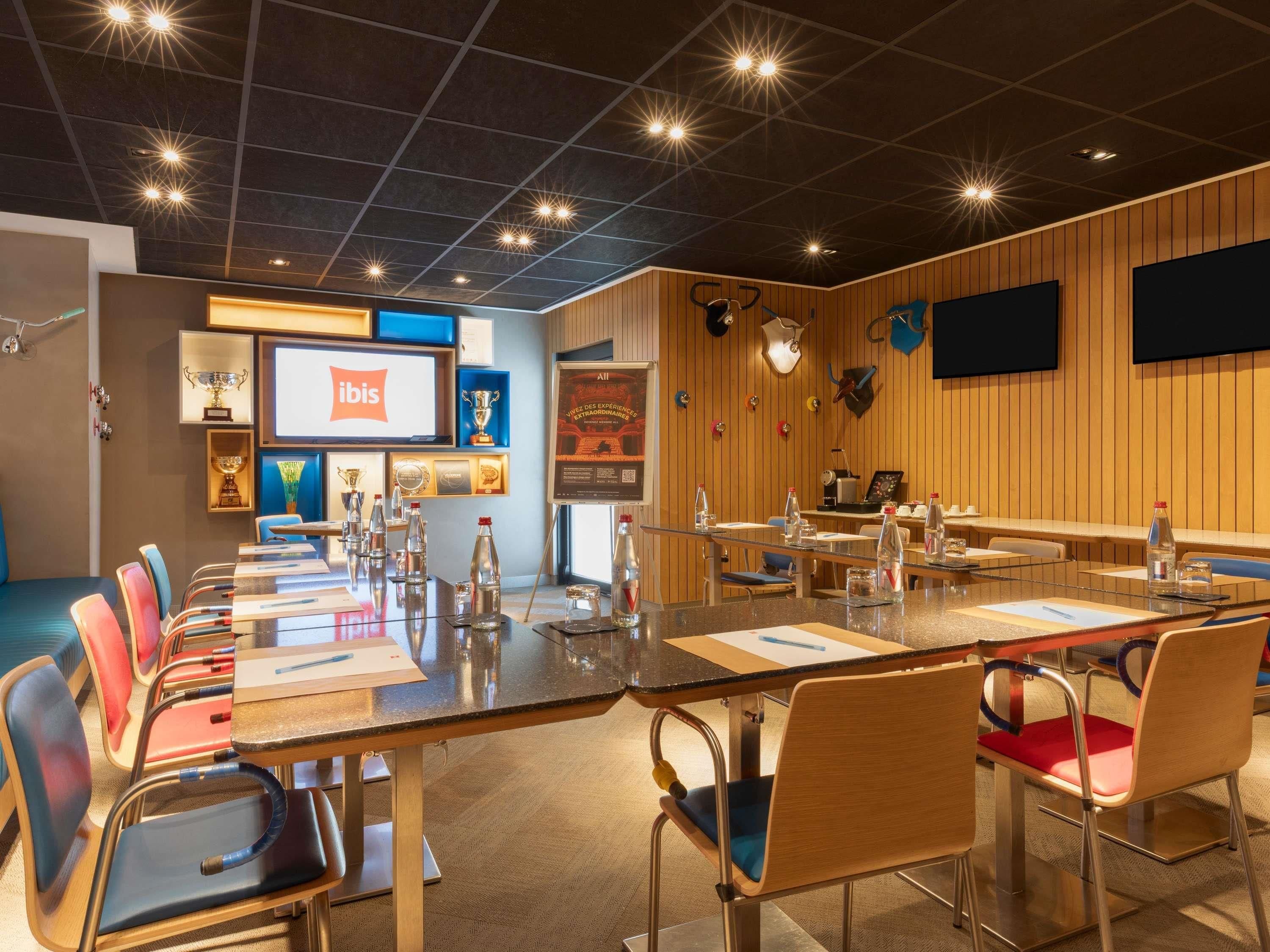 Une salle de conférence avec une longue table, des chaises et un écran affichant le logo d’Ibis.
