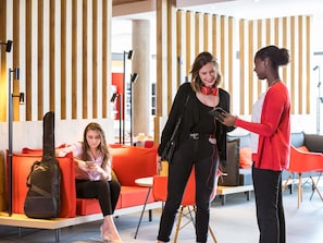 A modern interior with a wooden slat wall, red seating, and a person using a smartphone. - ibis Saint Quentin En Yvelines Velodrome (Montigny-le-Bretonneux)