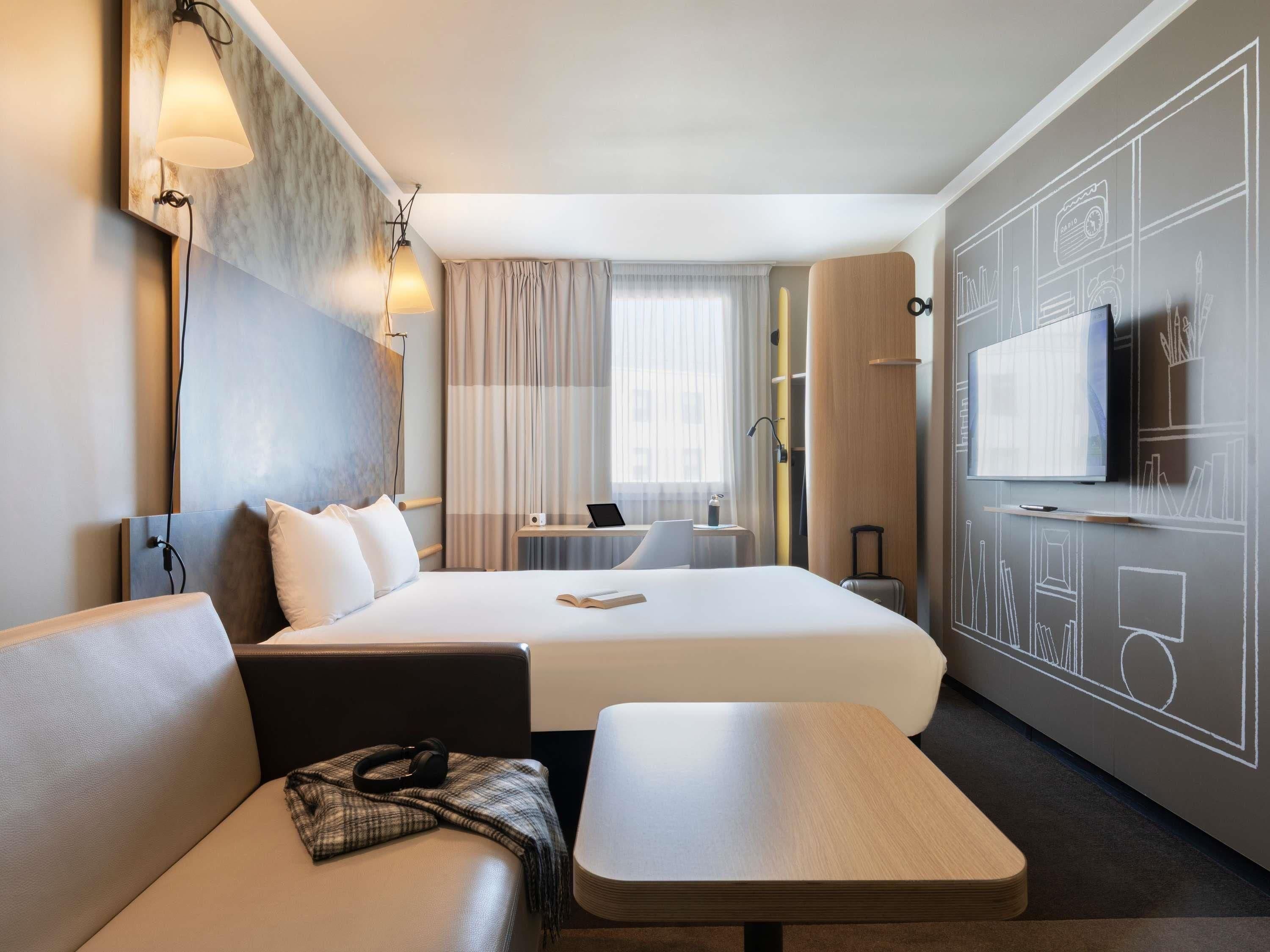 A hotel room with a bed, a desk, a TV, and a seating area.