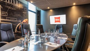 A conference room with a large table, chairs, and a screen displaying the ibis logo. - ibis Saint Quentin En Yvelines Velodrome (Montigny-le-Bretonneux)