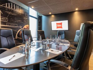 A conference room with a large table, chairs, and a screen displaying the ibis logo. - ibis Saint Quentin En Yvelines Velodrome (Montigny-le-Bretonneux)