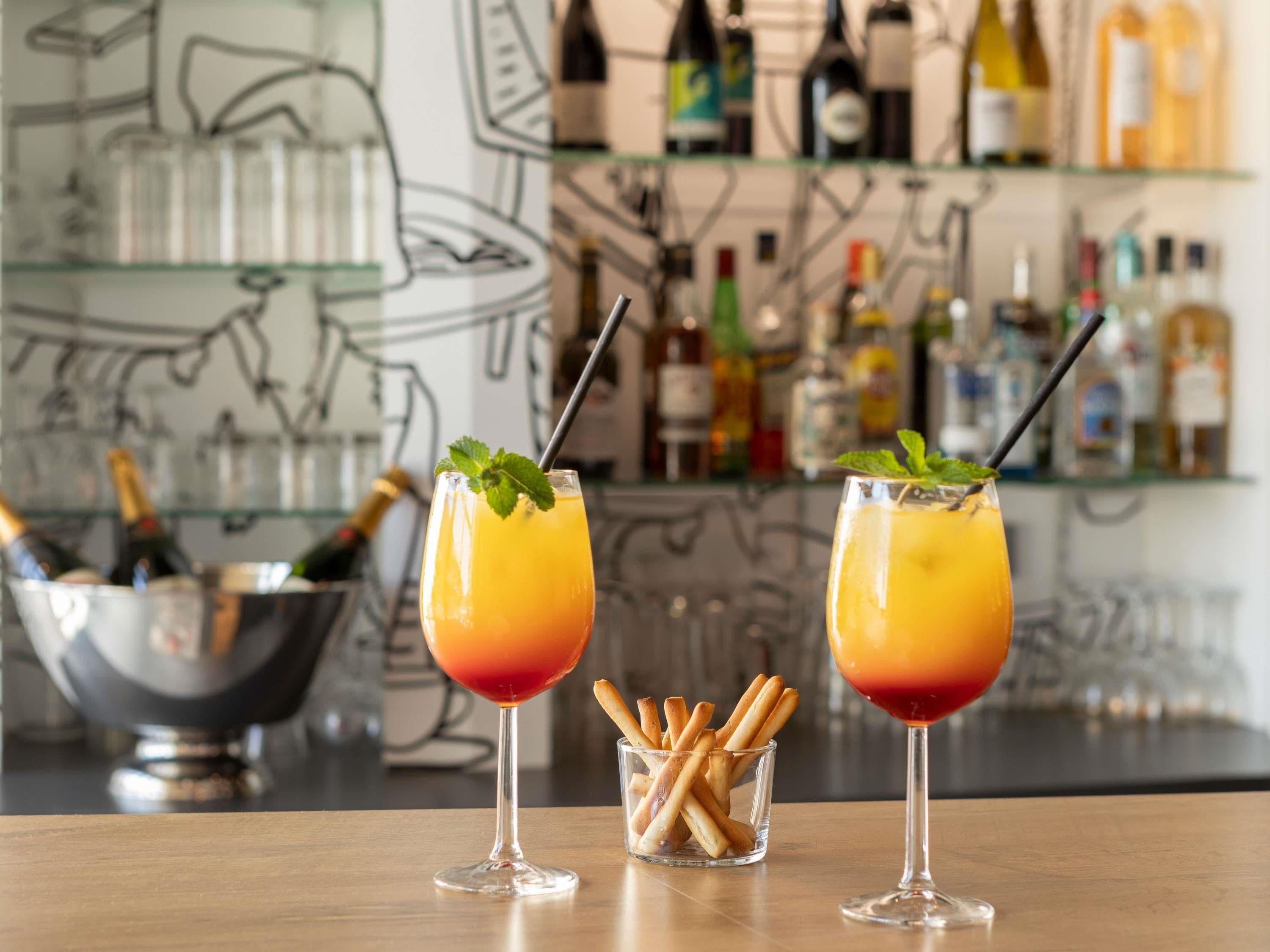 Zwei Cocktails mit Farbverlauf, ein Bierglas und eine Schüssel Brezeln auf einer Bar.