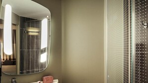 Ein Badezimmer mit einem großen Spiegel, einem Waschbecken, einem Handtuch und einer Dusche mit einer durchbrochenen Glasschiebetür.