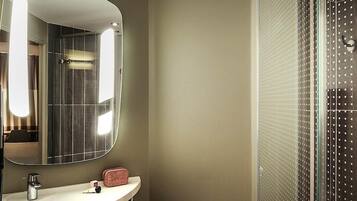 Een badkamer met een grote spiegel, een wastafel, een handdoek en een douche met een ruitpaneeldeur.