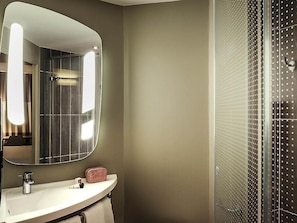 Ein Badezimmer mit einem großen Spiegel, einem Waschbecken, einem Handtuch und einer Dusche mit einer durchbrochenen Glasschiebetür.