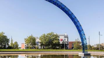A blue arched structure over a body of water with a reflection, a building with an 'ibis' sign, and trees in the background.