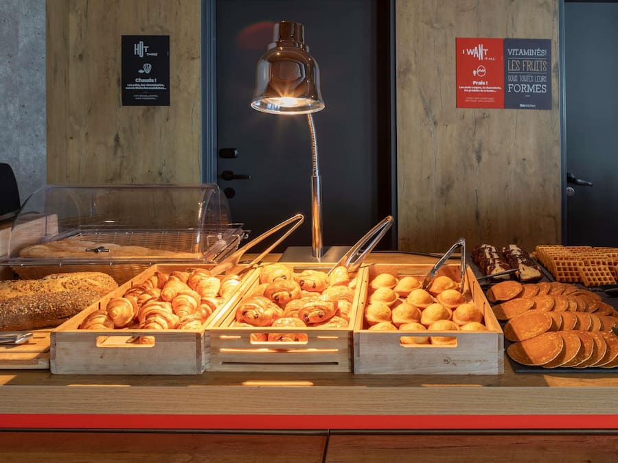 Un bufé de desayuno con diversos productos de panadería y un cartel que indica frutas gratis.