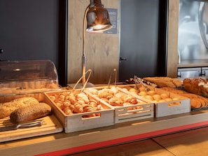 A bakery display with various baked goods, including bread and pastries, in a wooden counter setting. - ibis Saint Quentin En Yvelines Velodrome (Montigny-le-Bretonneux)