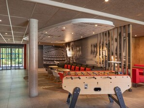 A spacious lobby with a foosball table, seating area, and a large mural. - ibis Saint Quentin En Yvelines Velodrome (Montigny-le-Bretonneux)