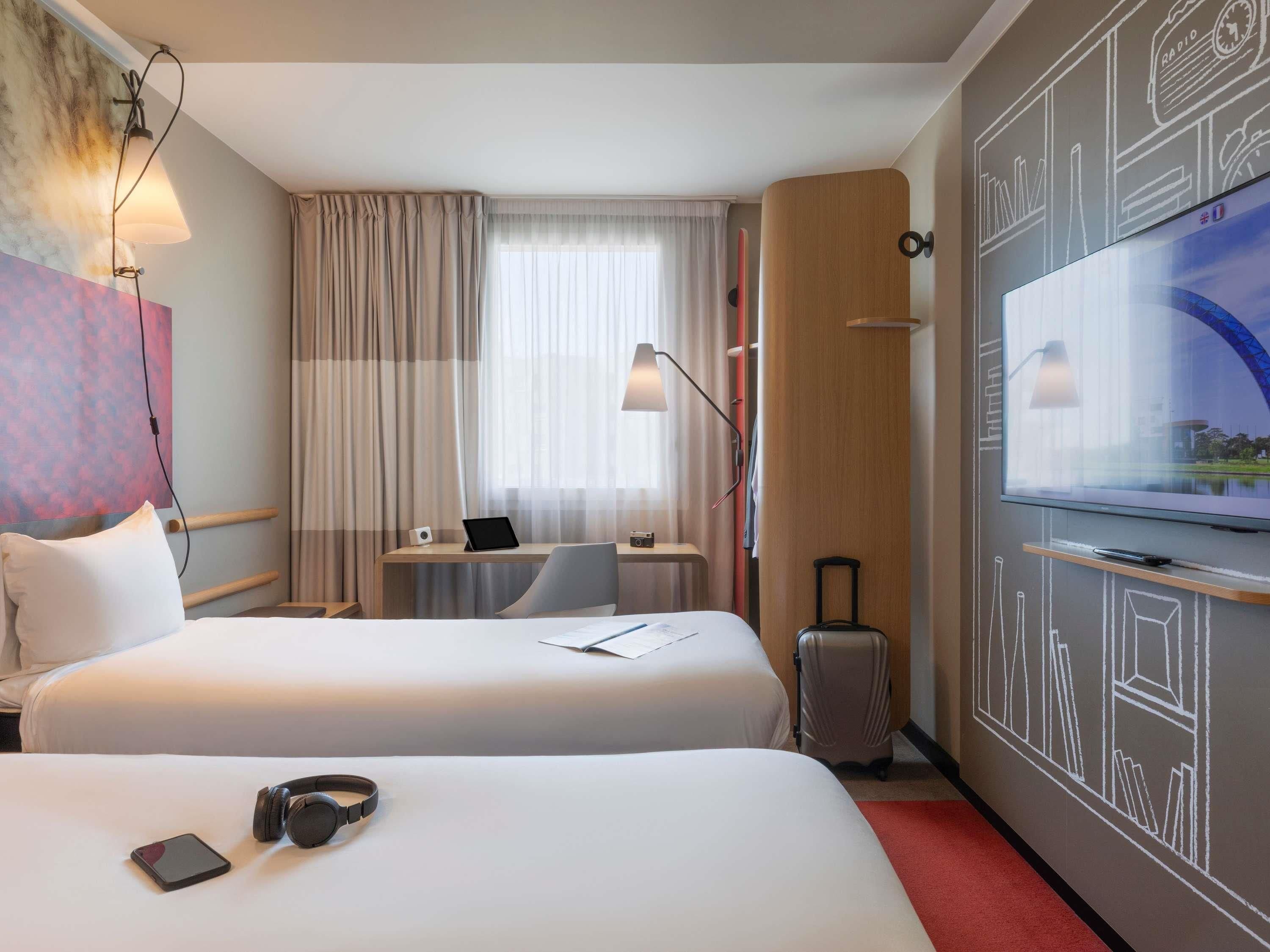A hotel room with two beds, a desk with a laptop, a television, and a suitcase.
