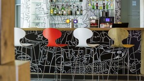 Eine Bar mit Wandgemälde in Schwarzweiß, Regalen voller Flaschen und modernen Stühlen.
