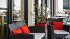 Ein moderner Außenbereich mit Korbmöbeln und roten Kissen, ein Blumentopf und Blick auf die Stadt durch große Fenster.