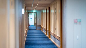 A hotel corridor with a blue carpet, wooden paneling, and a bench. - Travelodge Weston-super-mare (West Malling)