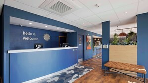 A reception area with a blue wall, a clock, and a reception desk. - Travelodge Weston-super-mare (West Malling)