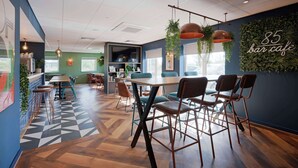 A modern bar cafe interior with wooden flooring, bar stools, and a large TV screen. - Travelodge Weston-super-mare (West Malling)