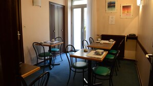 A dining area with tables and chairs, a door, and a window with curtains. - Hotel Du Lion (Vesoul)