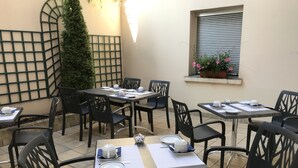 An outdoor dining area with tables and chairs, a decorative wall, and a window with flowers. - Hotel Du Lion (Vesoul)