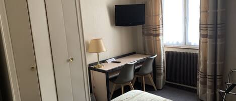 A hotel room with a bed, a desk with a chair, a television on the wall, and a window with curtains.