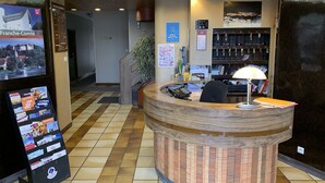 A reception desk with a wooden design, a digital display board, and a calendar on the wall. - Hotel Du Lion (Vesoul)