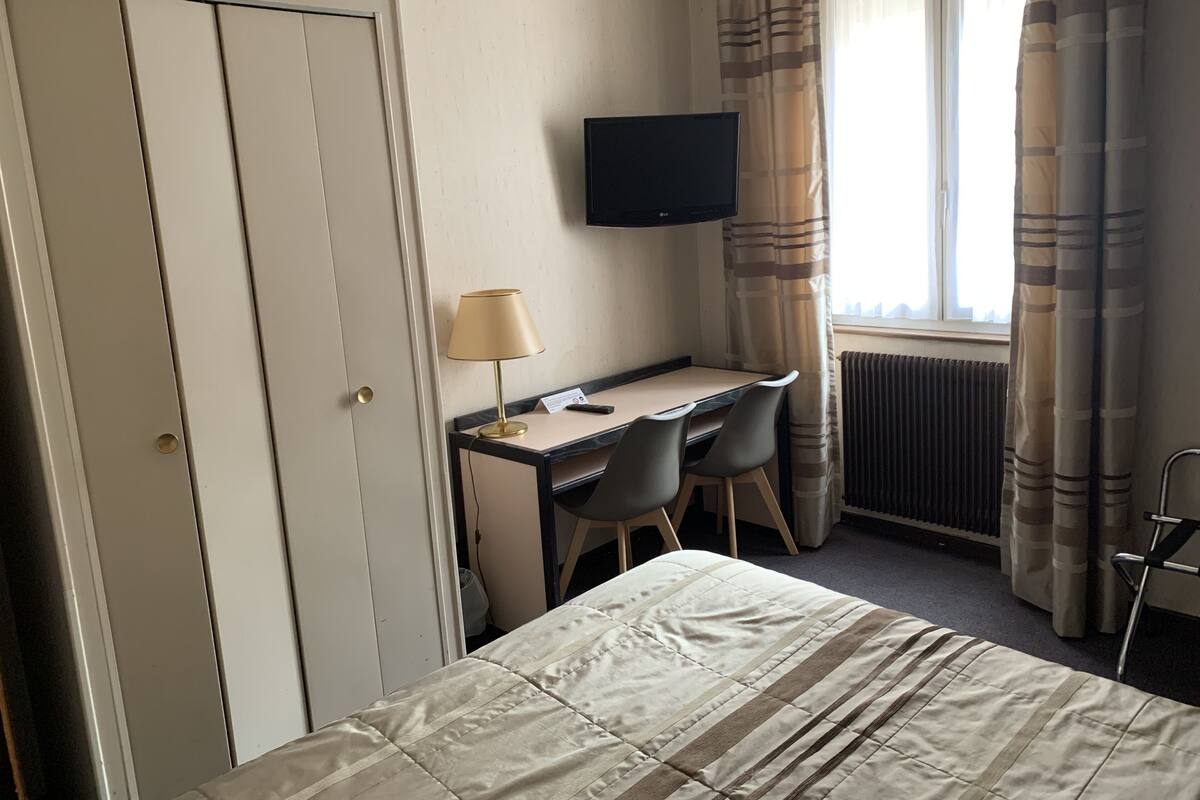 Hotellihuone, jossa on sänky, työpöytä tuolilla, seinälle asennettu televisio ja ikkuna, jossa on verhot.
