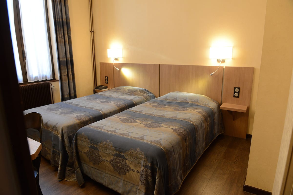 Hotellihuone, jossa on kaksi sänkyä, työpöytä ja yöpöytä.