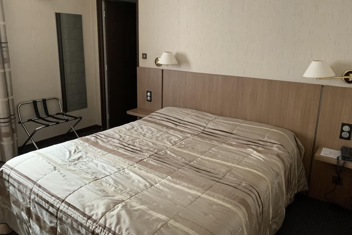 Hotellihuone, jossa on sänky, tuoli, peili ja kaksi seinään kiinnitettyä lamppua.