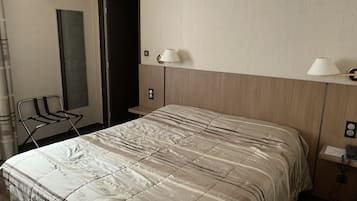 A hotel room with a bed, a chair, a mirror, and two wall-mounted lamps.