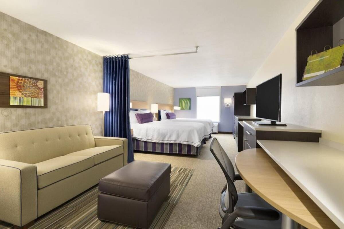 A hotel room with a bed, a sofa, a desk, a chair, and a TV.