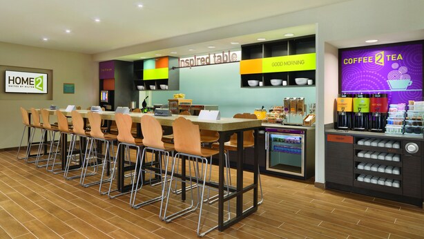 Un comedor de hotel con una larga mesa compartida, sillas, una estación de café y un cartel que dice 'Inspired table'.