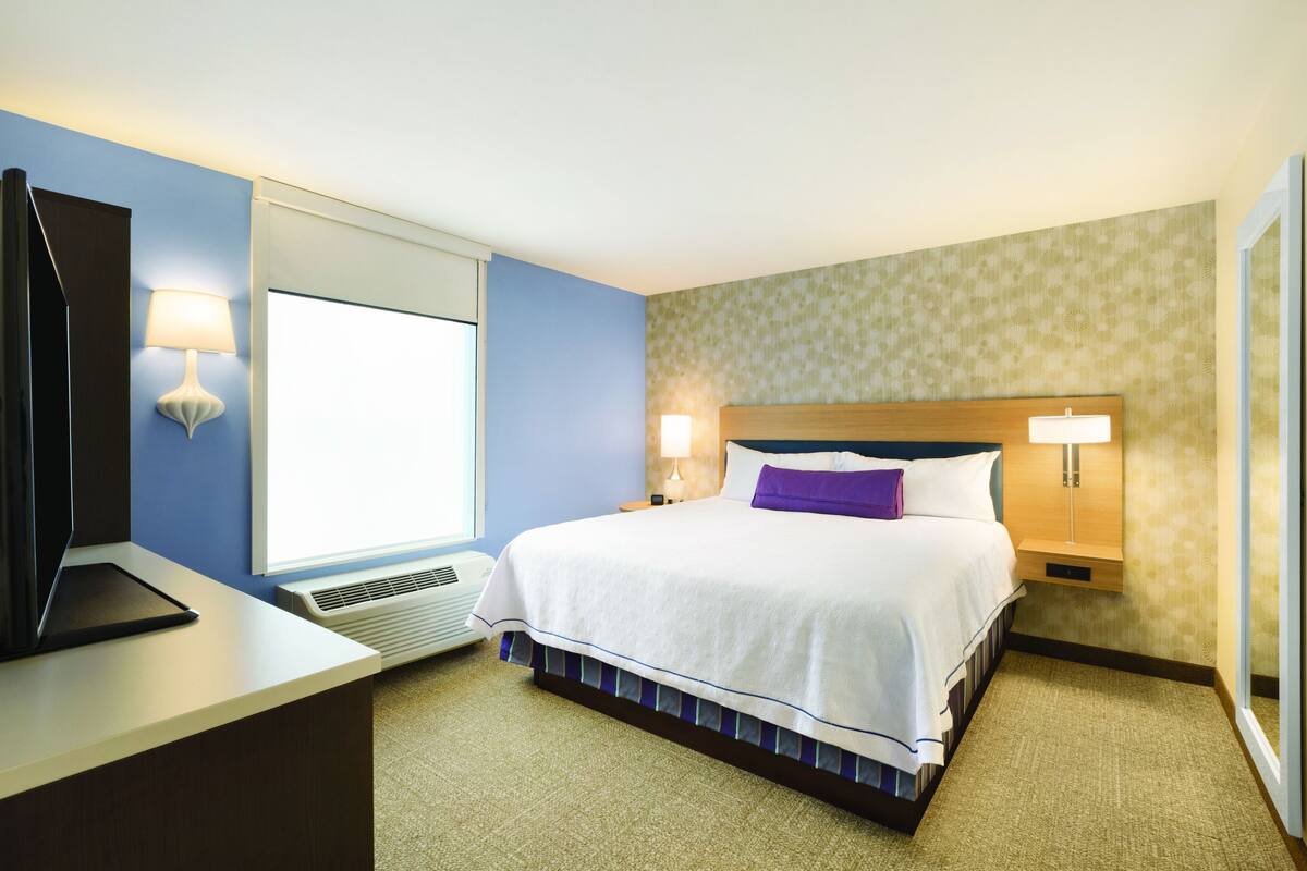 A hotel room with a bed, bedside lamps, a desk with a laptop, and a window.