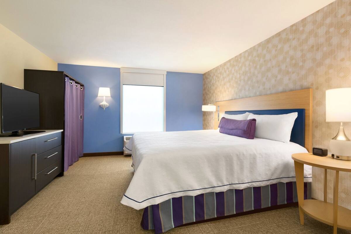 A hotel room with a bed, a TV, a desk, and a lamp.