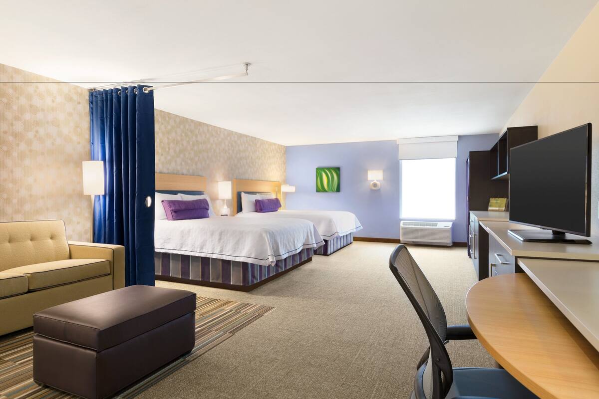 A hotel room with two beds, a sofa, a desk, and a television.