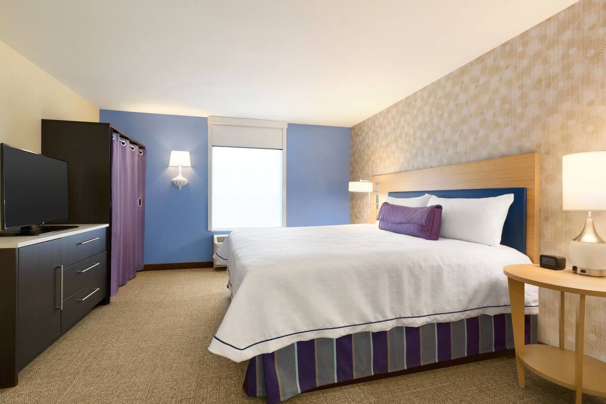 A hotel room with a bed, a TV, a desk, and a lamp.