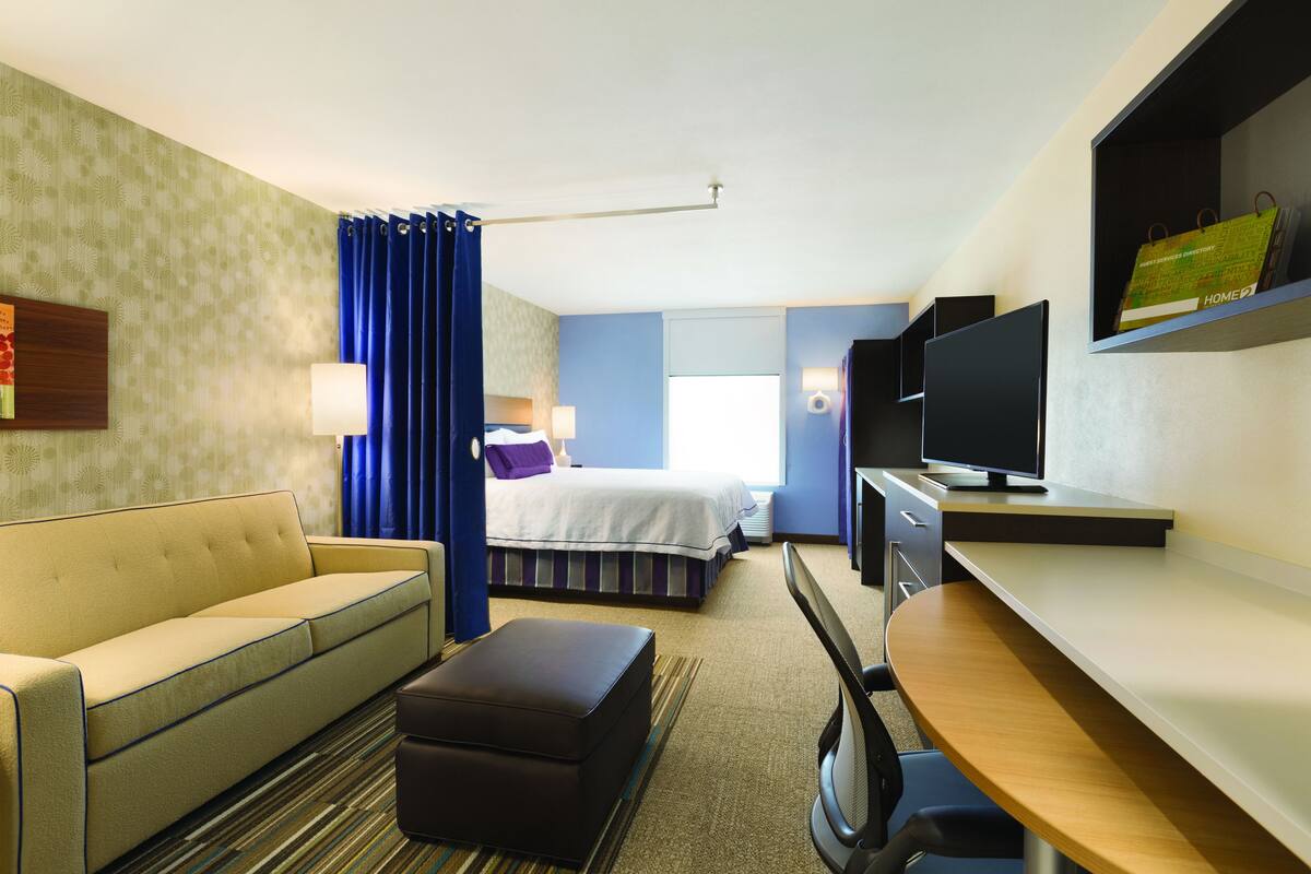 A hotel room with a bed, a sofa, a desk, a TV, and a bookshelf.