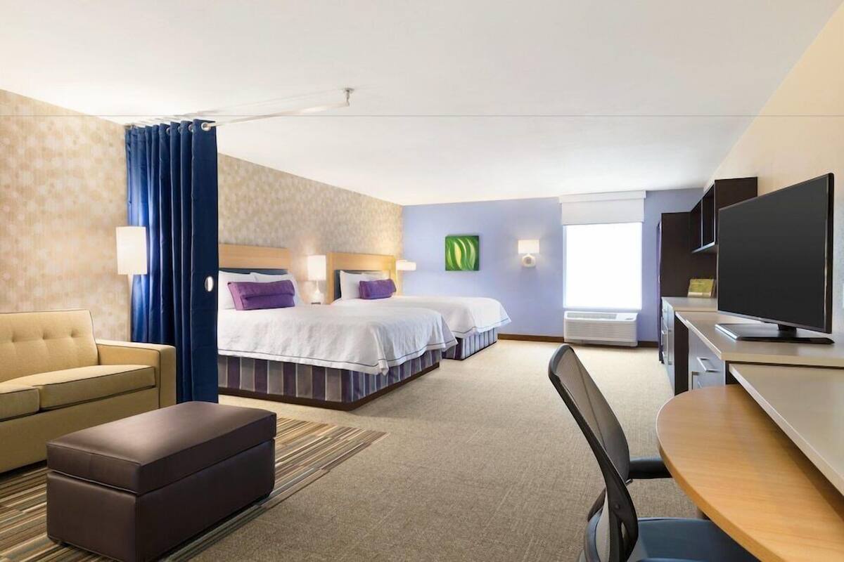 A hotel room with two beds, a sofa, a TV, and a desk.