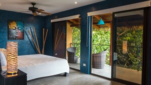 Un dormitorio con cama, ventilador de techo y vistas a un jardín exuberante a través de una puerta corrediza de vidrio.