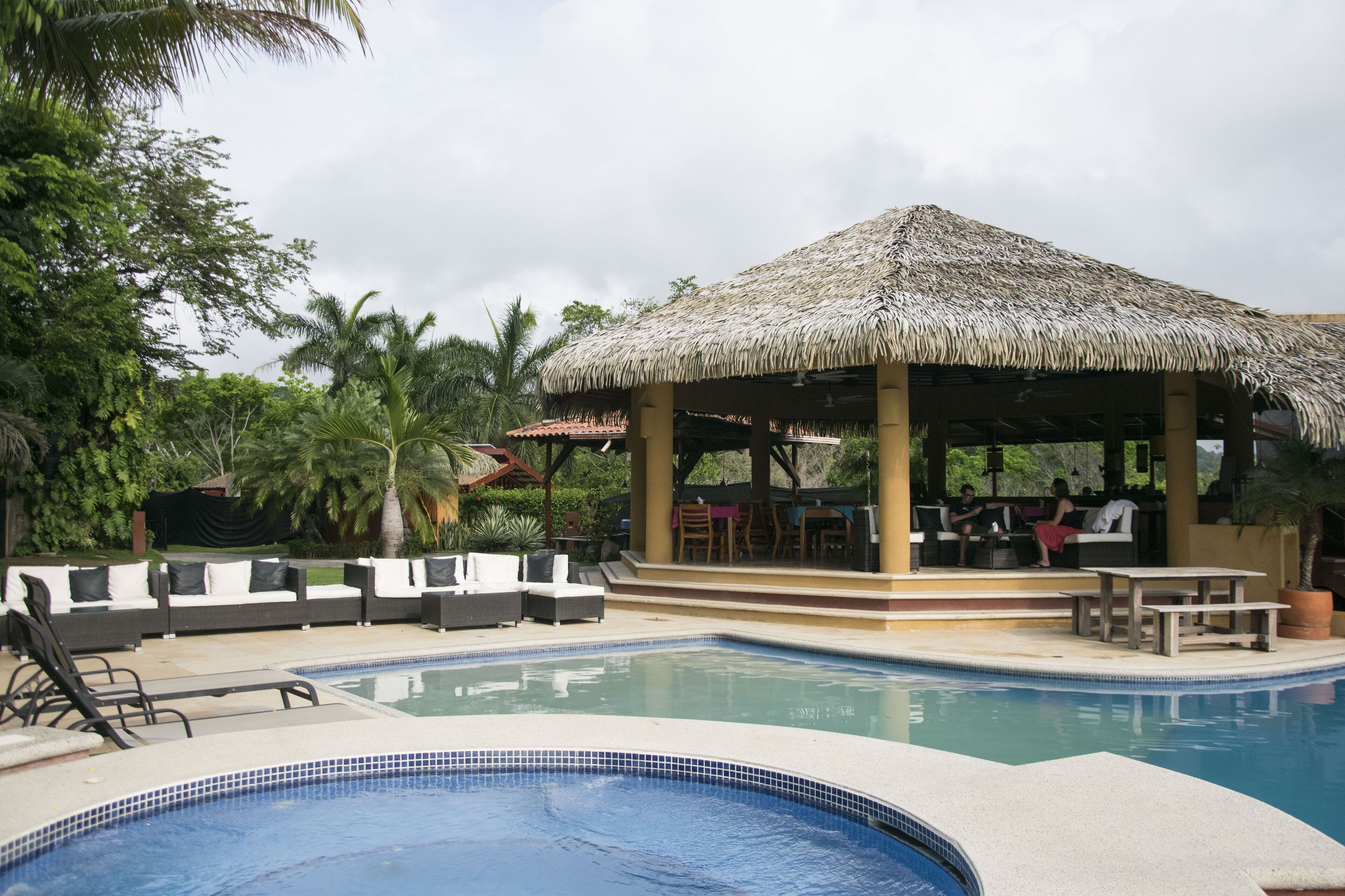 A pool area with lounge chairs and a thatched-roof pavilion.