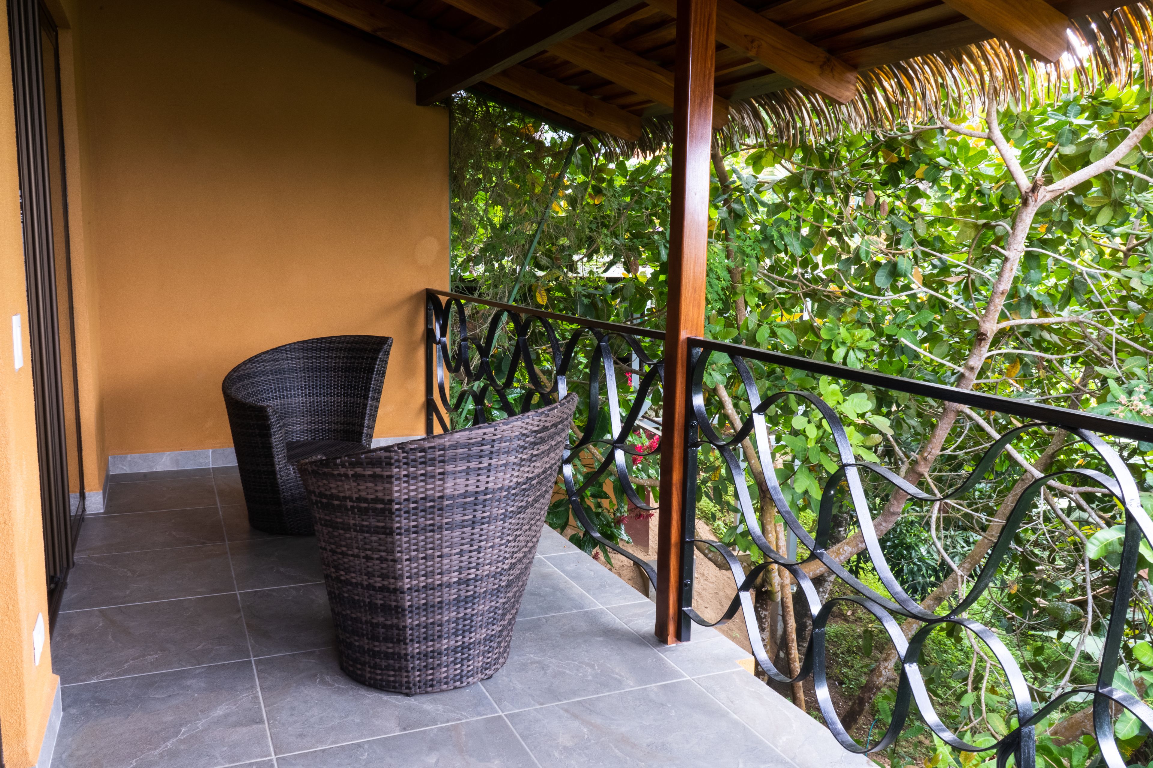 A balcony with wicker furniture and a metal railing overlooking a garden.
