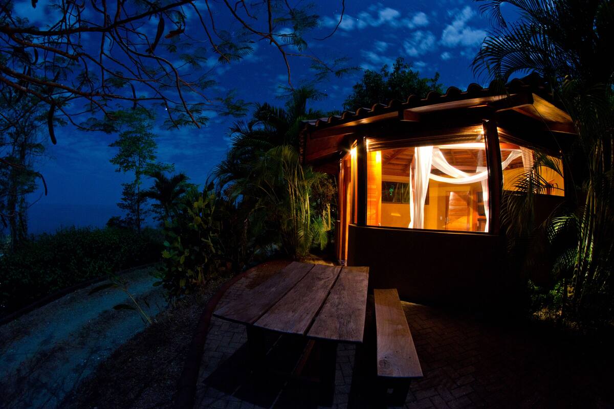 Une structure en bois dotée d’une porte en verre, entourée d’une végétation tropicale.