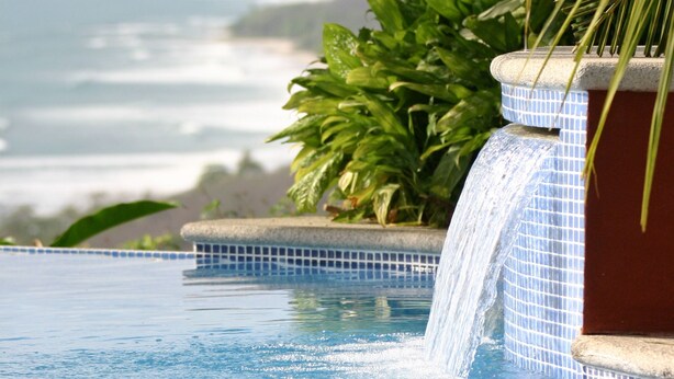 Una piscina con cascada, rodeada de abundante vegetación y vistas al océano.