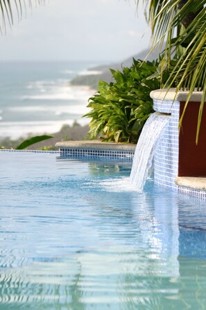 Una piscina con cascada, rodeada de abundante vegetación y vistas al océano.