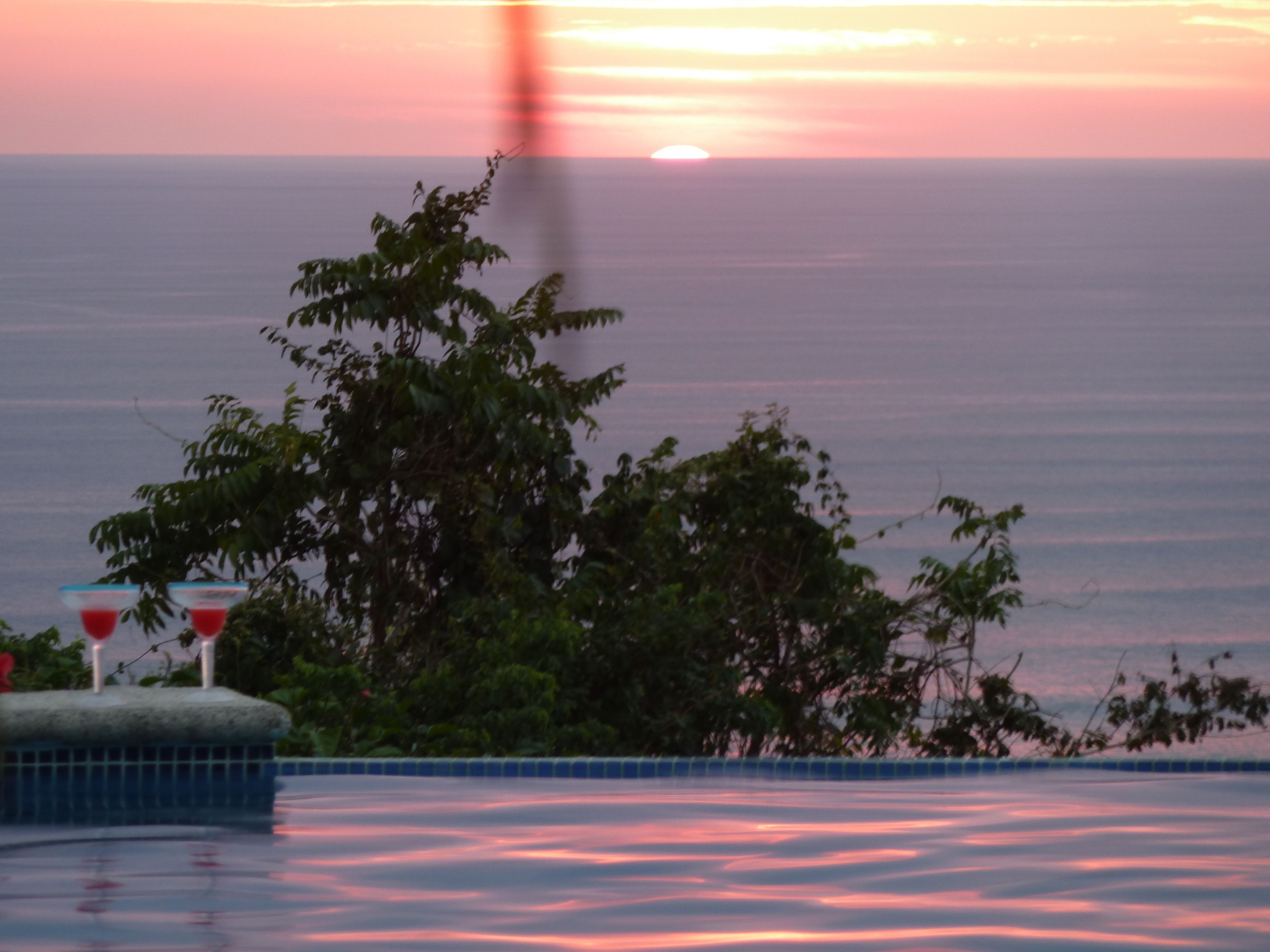 Un atardecer sobre un cuerpo de agua, con una piscina y árboles en primer plano.