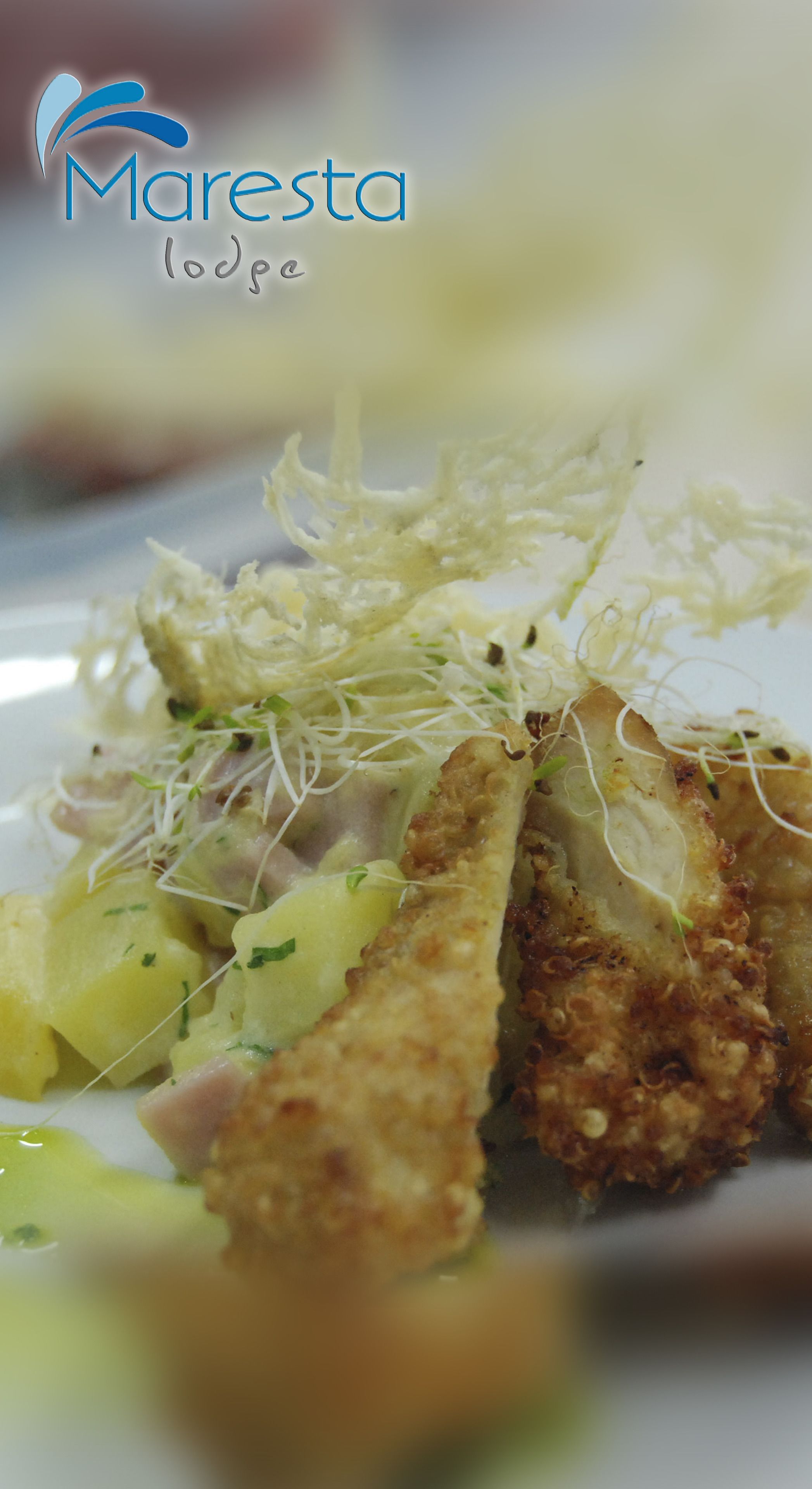 A close-up of a dish with breaded and fried items, possibly chicken, served with a side of potatoes and garnished with sprouts.