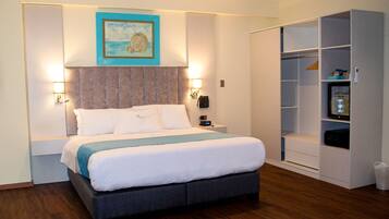 Habitación de hotel impecable con cama, lámparas de noche, un cuadro, armario y una mesita con un reloj.