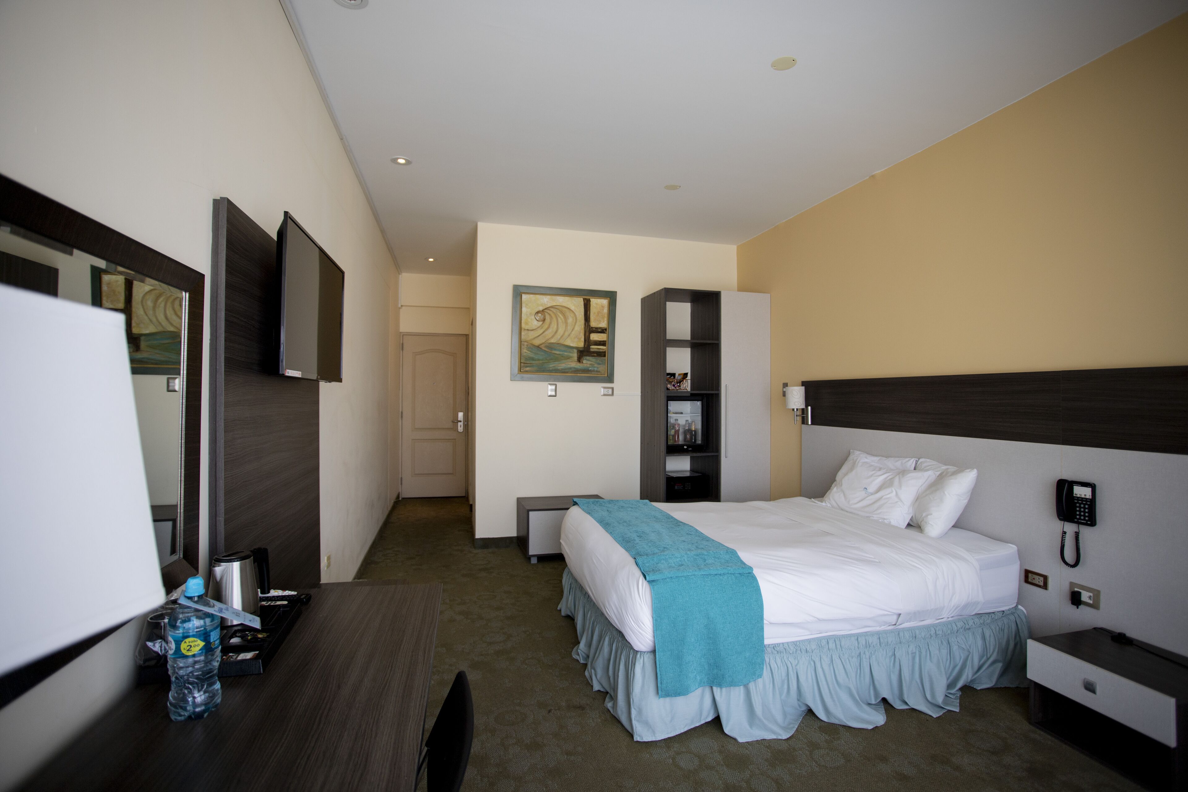 Een hotelkamer met een bed, nachtkastje, bureau, stoel en een grote spiegel.