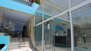Un hall d’hôtel moderne avec des portes vitrées, un comptoir d’accueil et un escalier menant aux étages supérieurs.